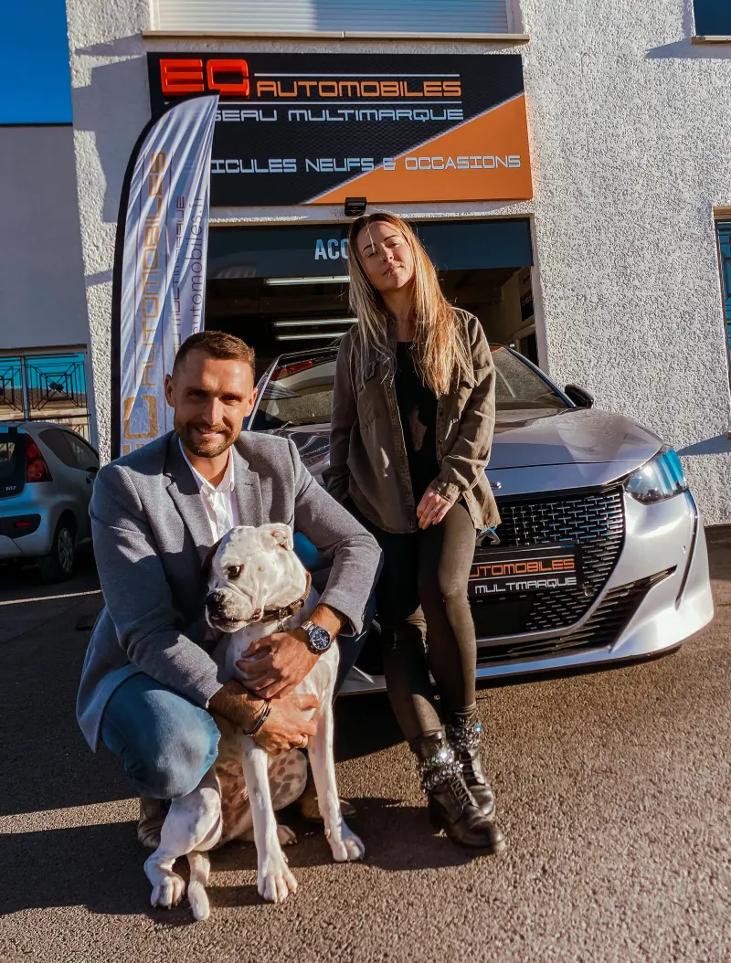 Un membre de l'équipe et une collègue, avec le chien du garage, devant la façade