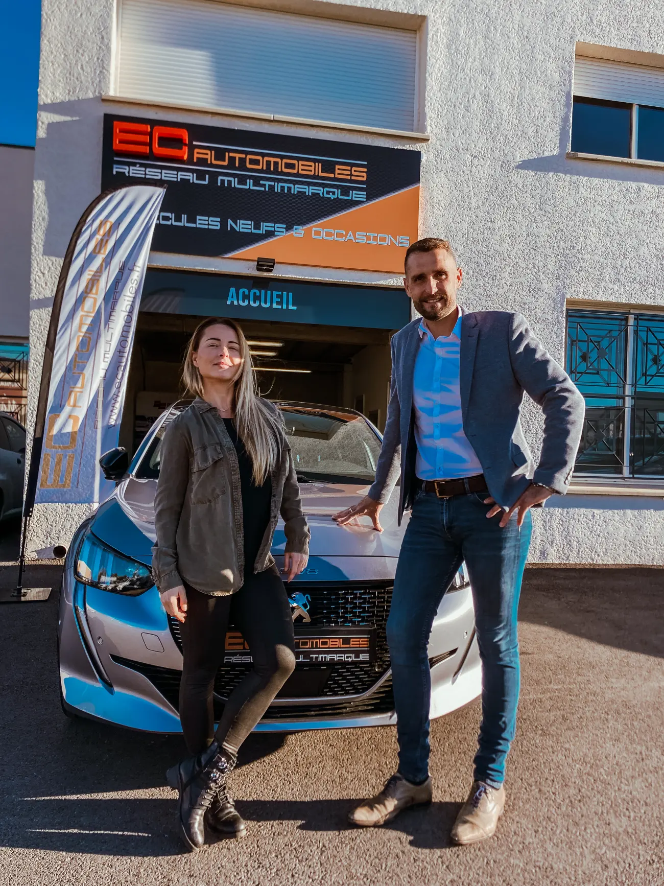 Deux membres de l'équipe d'EC Automobiles devant la façade du garage et une Peugeot 208